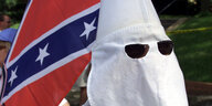 Ein Mitglied des Ku-Klux Klans mit seiner weißen Mütze und Sonnenbrille. Im Hintergrund die konföderierten Flagge