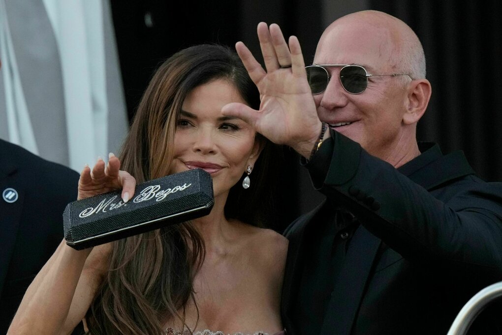 Lauren Sanchez Bezos (l) hält ein Etui mit der Aufschrift „Mrs. Bezos“, während Jeff Bezos winkt