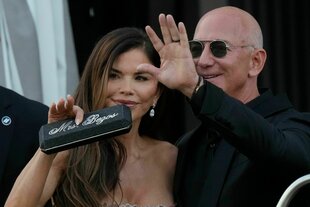 Lauren Sanchez Bezos (l) hält ein Etui mit der Aufschrift „Mrs. Bezos“, während Jeff Bezos winkt