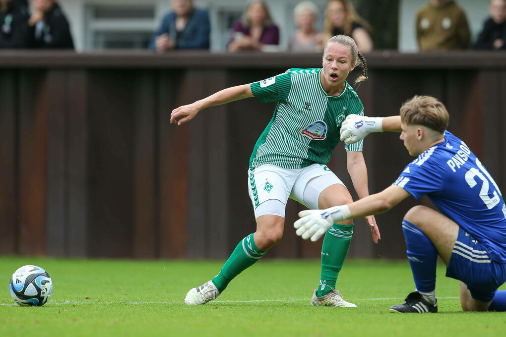 Eine junge Frau dribbelt einen Fußball am Torwart vorbei