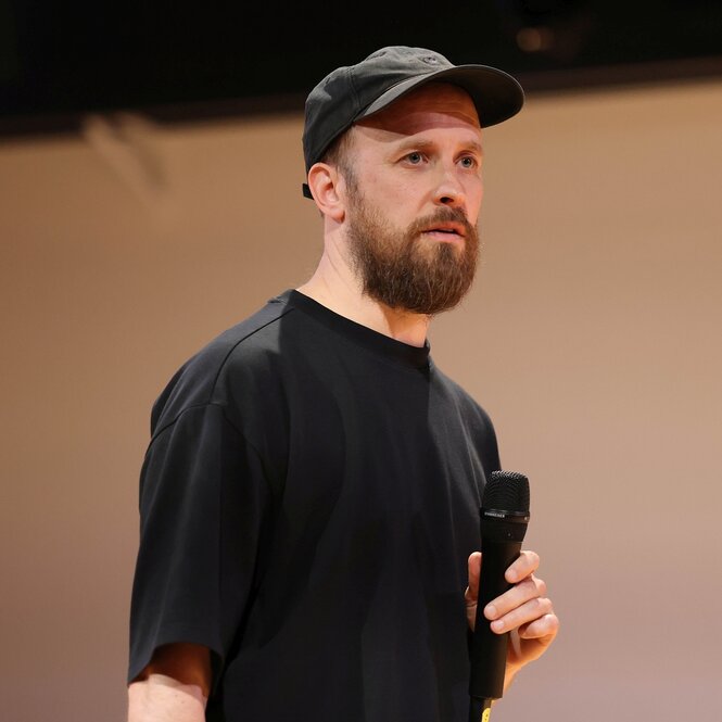Porträt von Moritz Ostruschnjak, mit schwarzem Basecap auf dem Kopf und Mikrofon in der Hand