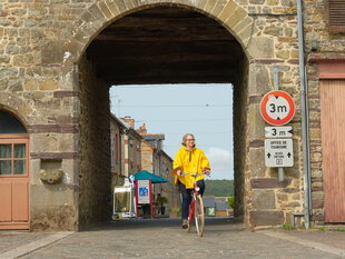 Joëlle Lesourd (Julie Delpy) mit Ostfriesennerz auf einem Fahrrad unter dem Stadttor einer namenlosen Ortschaft