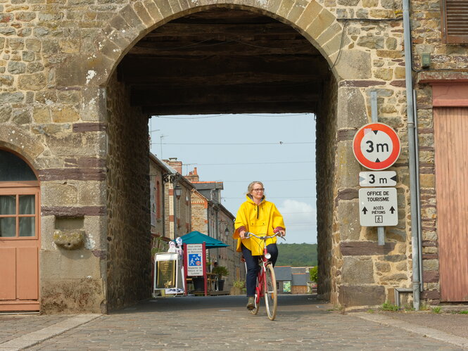 Joëlle Lesourd (Julie Delpy) mit Ostfriesennerz auf einem Fahrrad unter dem Stadttor einer namenlosen Ortschaft