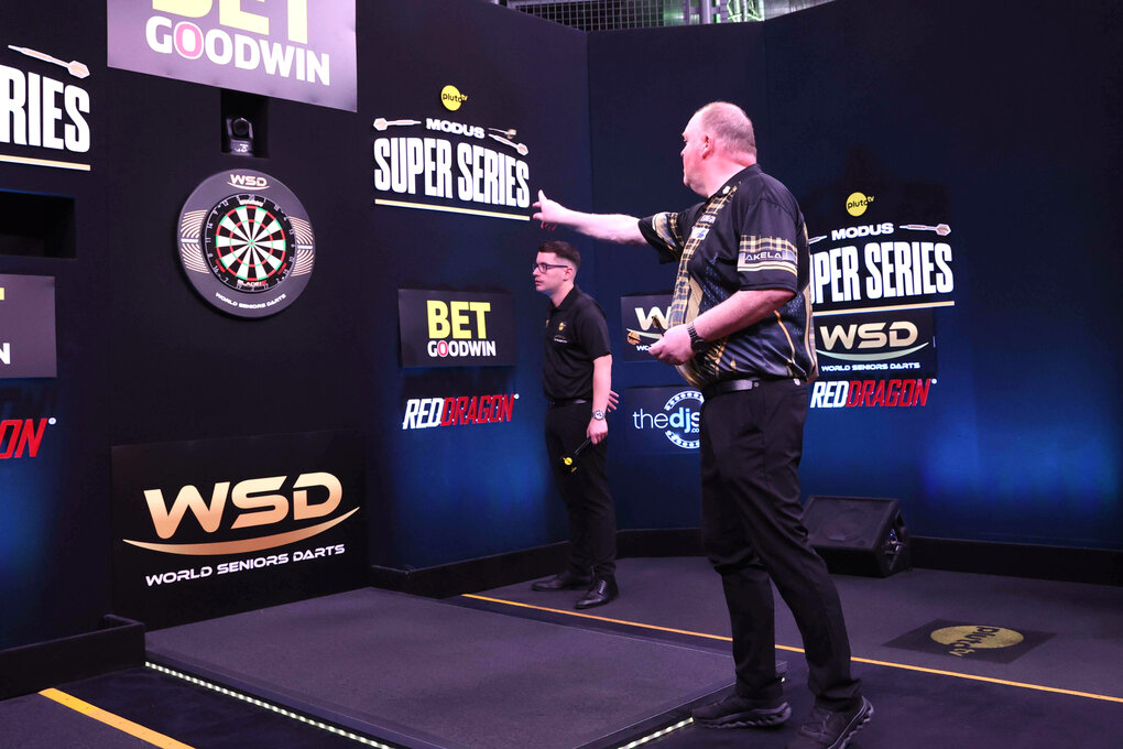 Darts-Turnier im englischen Portsmouth, Juni 2025 - Ein Mann wirft einen Pfeil Richtung Scheibe, das wird von einem weiteren Mann, der neben der Scheibe steht, beobachtet
