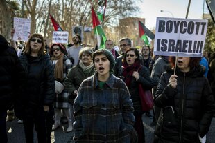 Protestaktion in Madrid, Protestierende - eine Frau hält ein Schild hoch mit der Forderung: Boykottiert Israel !!! Im Hintergrund sind palästinensische Flaggen zu sehen