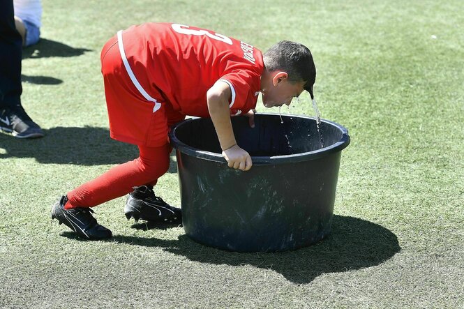 Ein Junge in roter Sportkleidung beugt sich nass über einen Wasserkübel