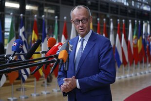 Friedrich Merz im blauen Anzug mit Krawatte steht vor vielen Mikrofonen vor europäischen Nationalflaggen beim EU-Gipfel. Sein Hände sind auf Bauchnabelhöhe ineinander verschränkt.