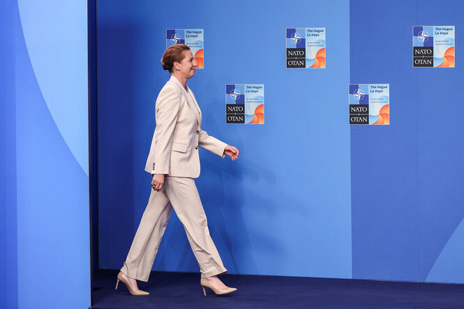 Mette Frederiksen geht im hellen Hosenanzug an einer blauen Wand vorbei, an der die Plakate zum Natogipfel angehängt sind