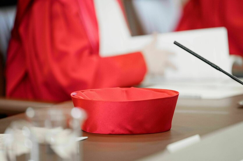 Die rote Kopfbedeckung eines Mitglieds des Bundesverfassungsgerichts liegt auf dem Tisch, im Hintergrund unscharf eine angeschnittene RichterIn