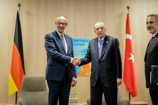 Friedrich Merz und Tayyip Erdogan schütteln sich die Hand beim Natogipfel - hinter ihnen die Fahnen Deutschlands und der Türkei