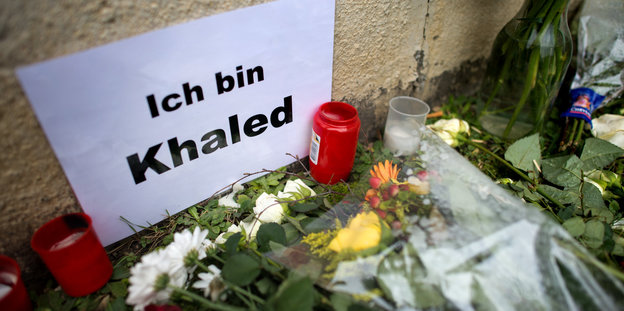 Kerzen und Blumen vor Zettel mit der Aufschrift „Ich bin Khaled“
