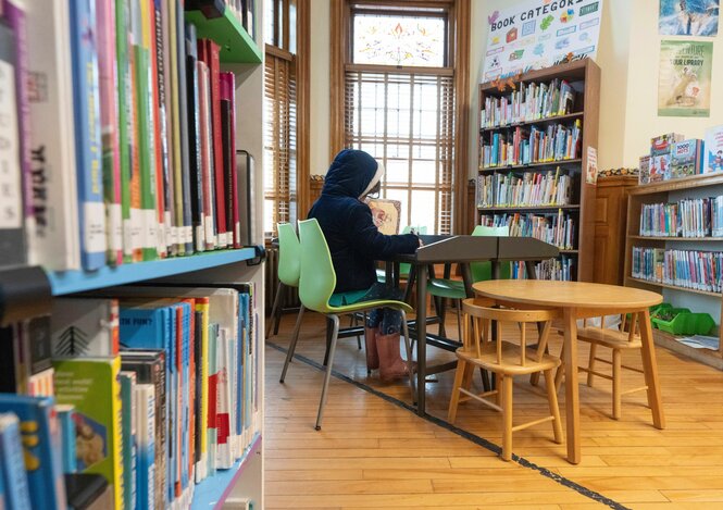 Ein Kind liest in einer Bibliothek, auf dem Fußboden eine schwarze Linie.