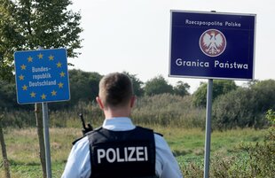 Ein deutscher Polizist steht zwischen den Grenzschildern von Deutschland und Polen