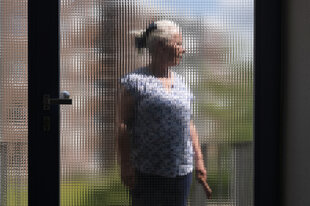 Eine Person ist anonymisiert hinter einer Scheibe fotografiert.