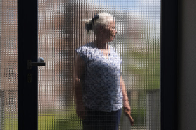 Eine Person ist anonymisiert hinter einer Scheibe fotografiert.