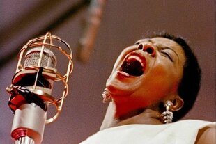 Ein Jazzsängerin steht auf einer Bühne und lehnt beim Singen den Kopf zurück, vor ihr steht ein goldenes Mikrofon