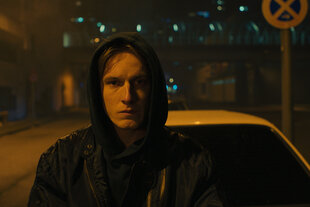 Kai (Louis Hofmann) steht im Hoodie nachts vor einem Auto auf der Straße.