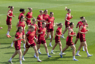 Junge Frauen in roten Trikots wärmen sich auf einem Fußballplatz auf