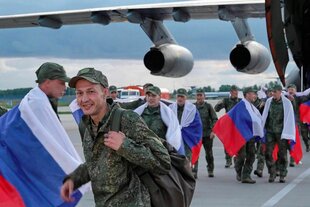 Russische Soldaten verlassen mit Nationalflaggen ein Flugzeug