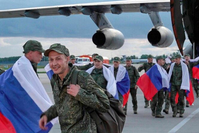Russische Soldaten verlassen mit Nationalflaggen ein Flugzeug