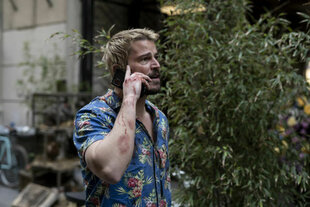 Lucas Reyes (Josh Hartnett) steht mit Mobiltelefon neben einem Busch.