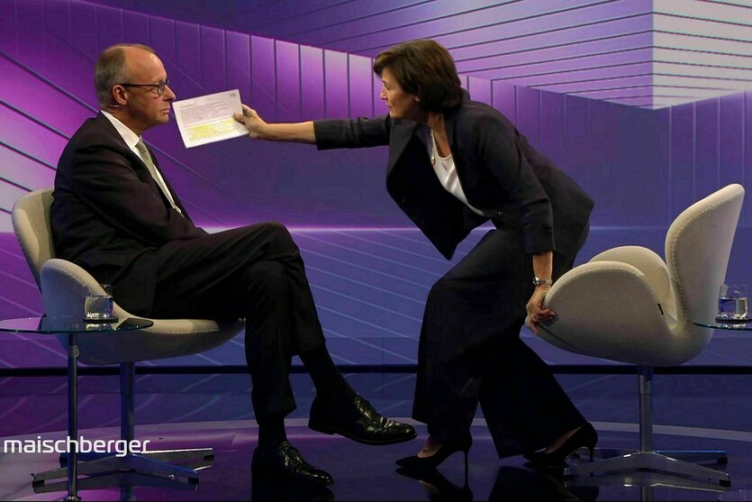 Sandra Maischberger sitzt Friedrich Merz im Fernsehstudio gegenüber und fuchtelt Merz mit einem Blatt Papier im Gesicht herum