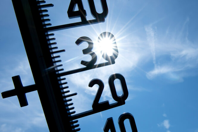 Ein schwarzes Thermometer vor blauem Sonnenhimmel