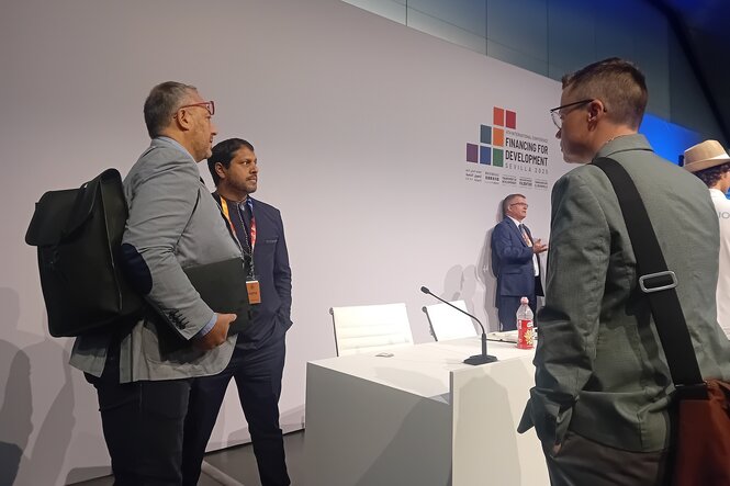 Jason Rosario Braganza steht am Rande der Bühne eines Gesprächspanels, er unterhält sich mit anderen Leuten