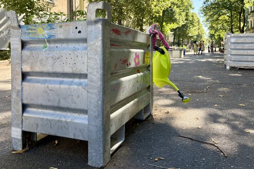 Hochbeet aus Metall mit Gießkanne auf einer sonnenbeschienenen Straße