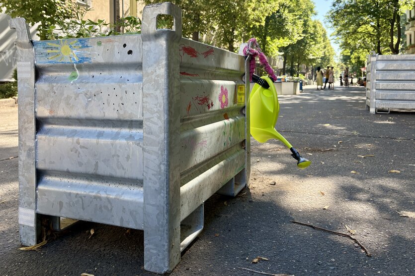 Hochbeet aus Metall mit Gießkanne auf einer sonnenbeschienenen Straße