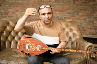 Ozan Ata Canani sitzt mit seiner Saz auf einem Ledersofa