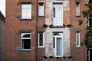 Ramponierte Fassade eines Backsteinhauses mit ausgerissenen Balkonen.
