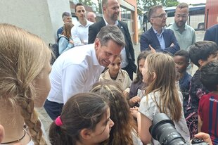 Lies im weißen Hemd bückt sich hinunter zu Kindern und spricht mit ihnen