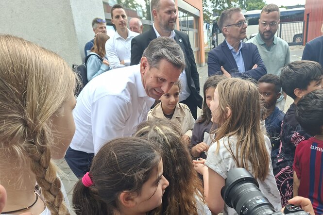 Lies im weißen Hemd bückt sich hinunter zu Kindern und spricht mit ihnen