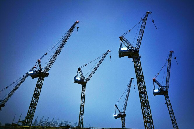Fünf Kräne vor blauem Himmel, unten sind die Stahlbetonpfähle eines Neubaus zu sehen