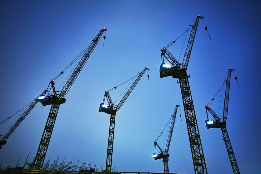 Fünf Kräne vor blauem Himmel, unten sind die Stahlbetonpfähle eines Neubaus zu sehen