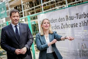 Verena Hubertz (SPD) steht mit Lars Klingbeil am Rand einer Baustelle, ein Transparent verkündet den Bau-Turbo und sie krempelt die Ärmel hoch