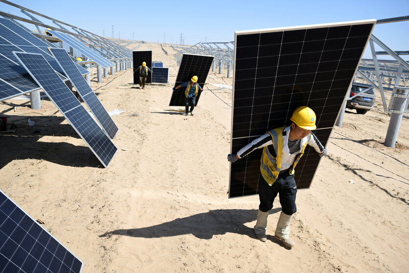 Feld mit Solarpanelen in China, Arbeiter tragen auf dem Rücken einzelne Panele das Feld entlang