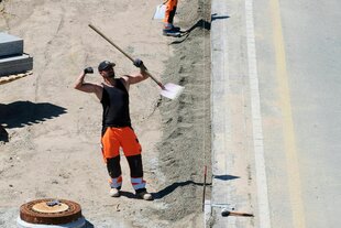 Ein Bauarbeiter steht mit einer Schaufel aneiner Straße und reckt die Fäuste Richtung Sonne