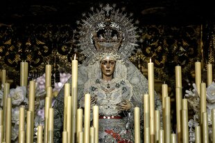 Die Statue der Macarena in einem prächtigen hellenGewand mit Perlen, einer Monstranz auf dem Kopf und Tränen auf der Wang, davor stehen weisse Kerzen