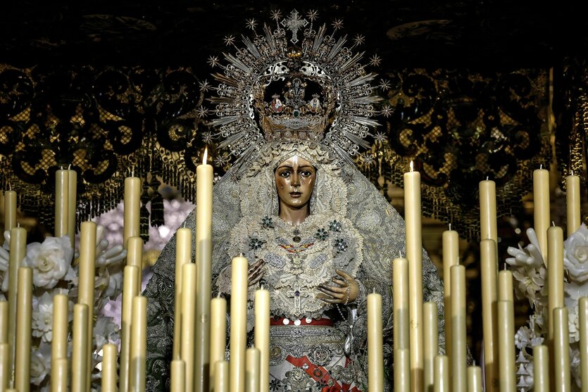 Die Statue der Macarena in einem prächtigen hellenGewand mit Perlen, einer Monstranz auf dem Kopf und Tränen auf der Wang, davor stehen weisse Kerzen