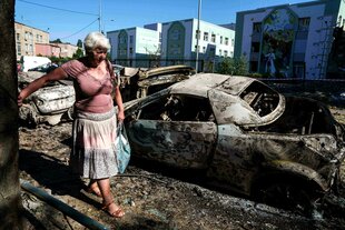 Eine Einheimische geht an Autos vorbei, die durch einen russischen Angriff zerstört wurden.