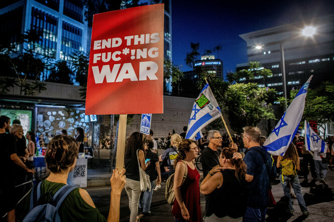 Demonstranten halten bei einer Antikriegsdemonstration die israelische Flagge und ein Plakat mit der Aufschrift "End This Fuckin War" hoch