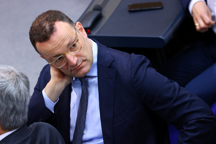 Jens Spahn sitzt im Bundestag und neigt seinen Kopf zur rechten Seite und fasst sich mit der rechten Hand ans Gesicht