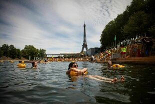 Menschen genießen das Wasser an der sicheren Badestelle Grenelle an der Seine in Paris, Frankreich, während der Eröffnung der drei Seine-Schwimmbecken. Im Hintergrund der Eiffelturm.