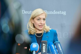 Eine Frau mit blauer Jacke spricht zu Vertretern der Presse