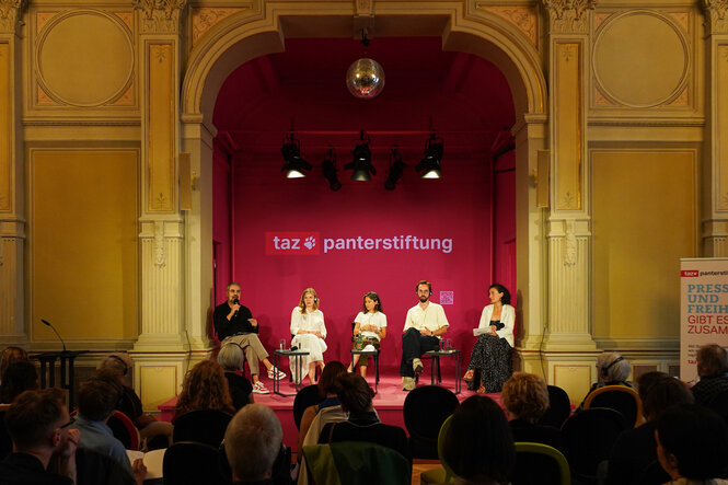 Eine Diskussion der taz Panter Stiftung im großen Saal des Deutschen Theaters Berlin, fotografiert aus mittlerer Distanz. Vor großem Publikum sitzt eine fünfköpfige Gruppe auf einer kleineren Bühne.