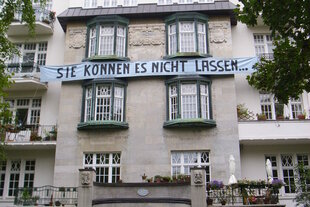 Die Fassade eines Altbaus. Auf einem Transparent steht: "Sie können es nicht lassen..."