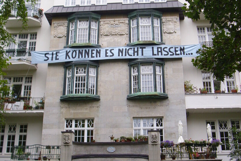 Die Fassade eines Altbaus. Auf einem Transparent steht: "Sie können es nicht lassen..."
