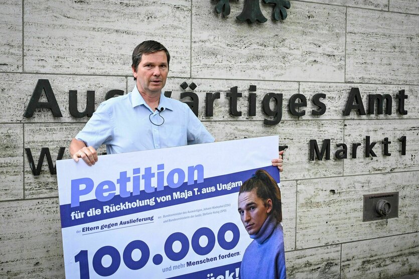 Wolfram Jarosch steht vor dem Gebäude des Auswärtigen Amtes und hält ein Plakat mit der Aufschrift "Petition" in den Händen